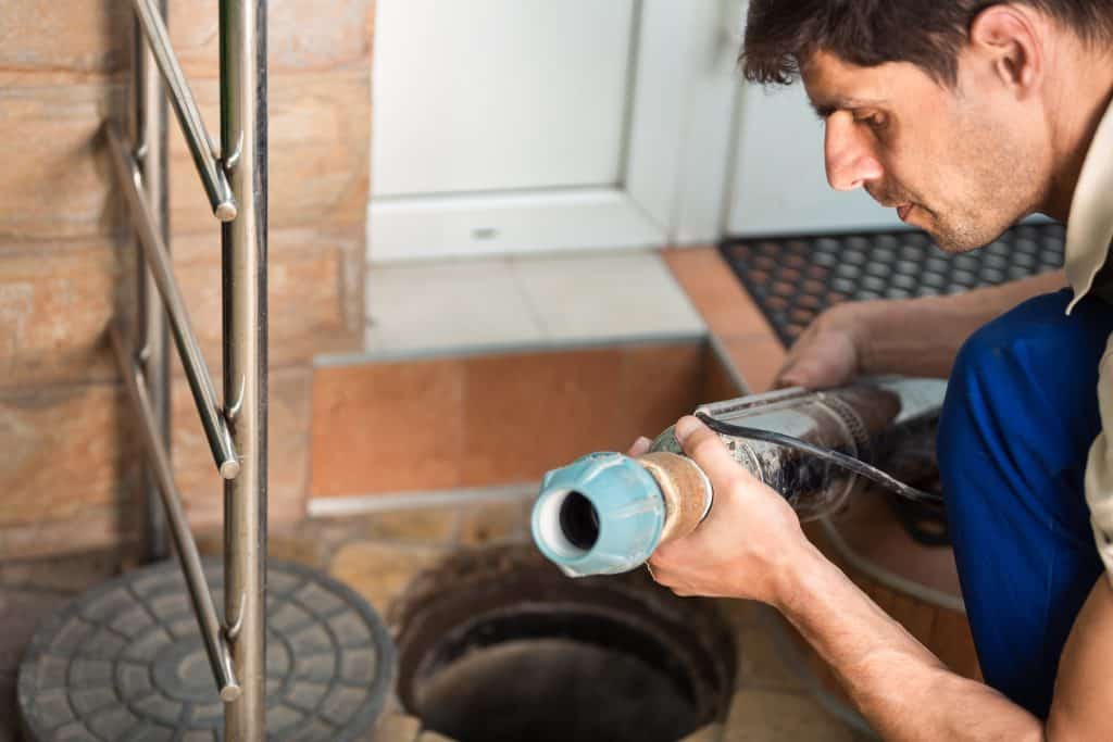 A plumber from the best Chicago plumbing company kneels near an open drain, inspecting a large pipe. The setting is close to a building entrance with a tiled floor and a doormat in the background. He remains focused on his work, exemplifying why he's part of the top team in plumber Chicago services.