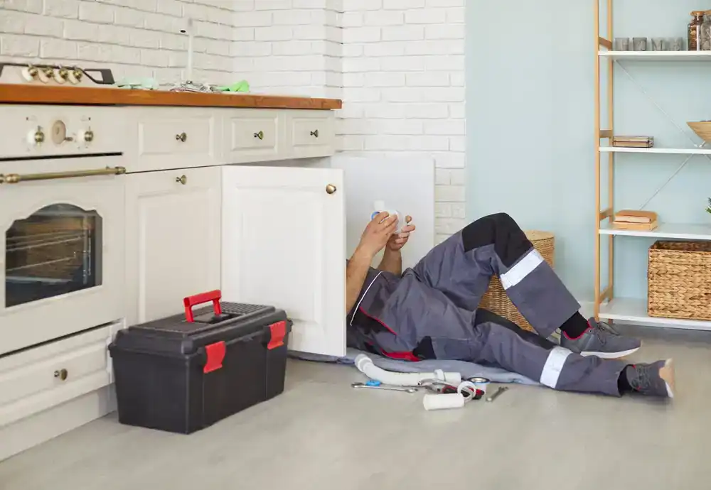 Plumber in Cook County, Illinois repairing under a kitchen sink, using tools to fix pipes and ensure proper water flow, demonstrating professional plumbing services