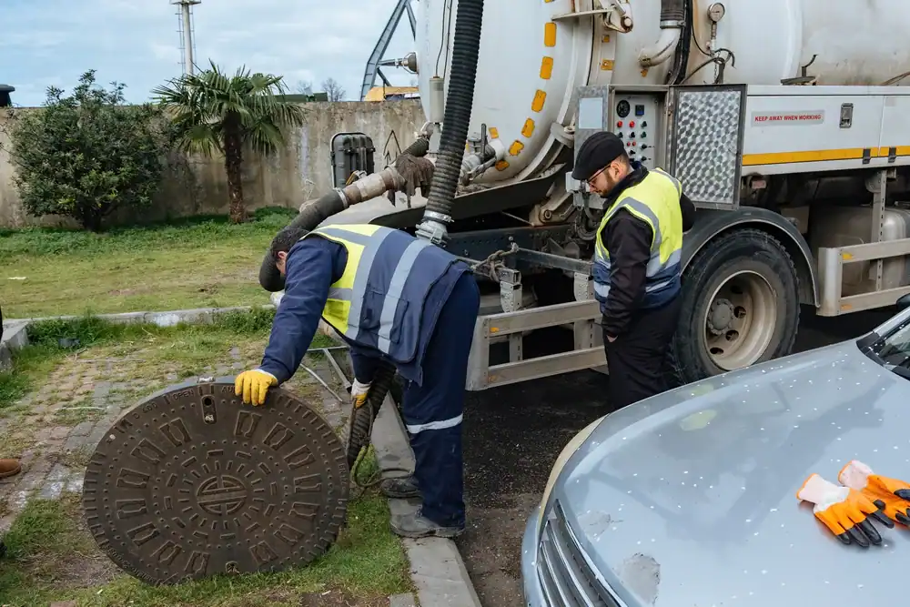 Workers performing manhole maintenance on a city street, wearing safety gear and using professional equipment, showcasing All Rooter Hydro Jetting experts at work
