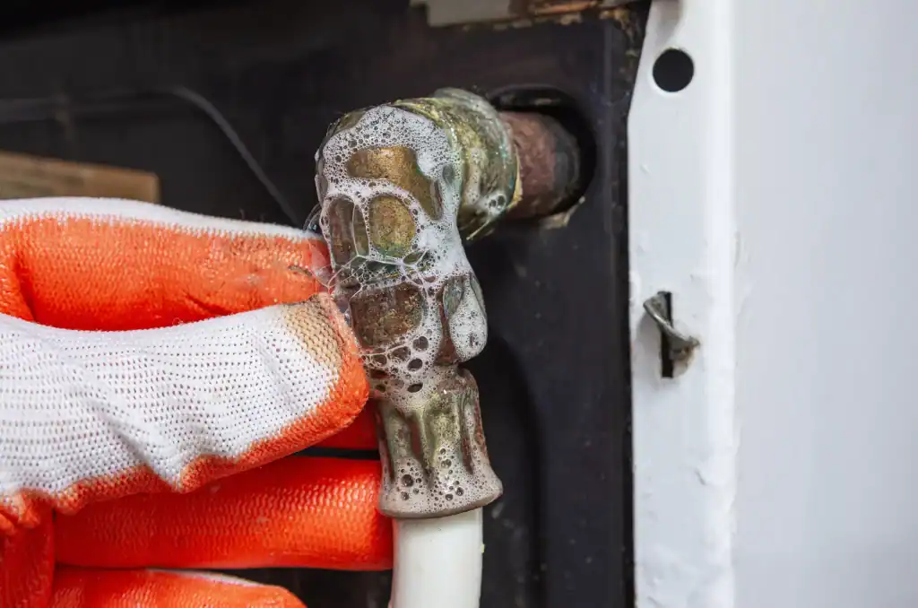 A gloved hand holds a metal pipe connection with soap bubbles, indicating a gas leak detection test by a plumber in Chicago, IL.
