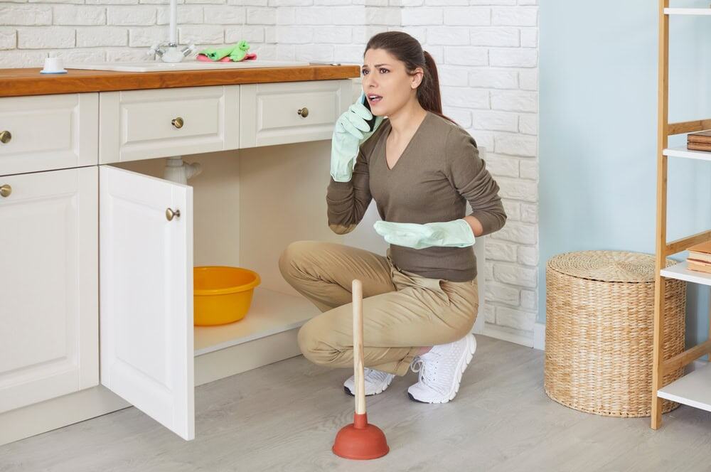 Frustrated homeowner on phone dealing with clogged kitchen sink causing household plumbing problem